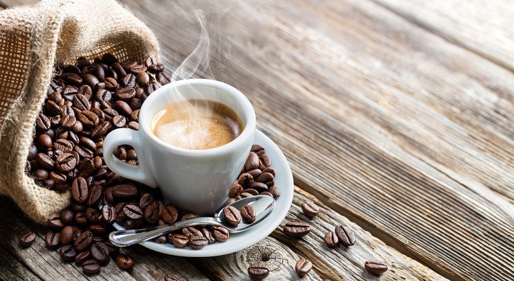 Une tasse de café entouré de quelques grains de café sur une table en bois.