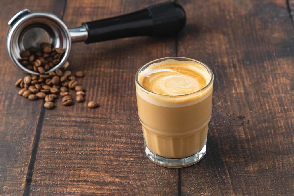 Un café Cortado préparé dans une tasse en verre sur une table en bois.