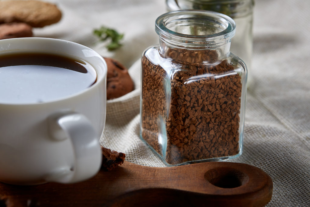 Café instantané dans une tasse blanche et à côté les grains déjà moulu prêt à être déposé dans l'eau chaude.