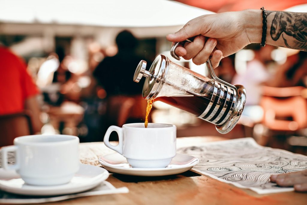 Presse française à moitié remplie de café versée dans une tasse de café muni d'une soucoupe. 