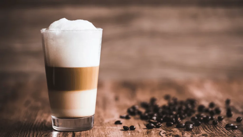 Un café Macchiato préparé avec quelques grains de café sur le côté.